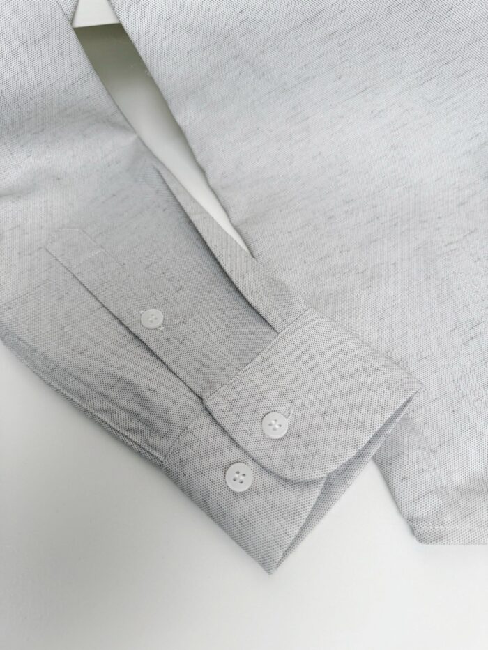 Dettaglio di un polsino di camicia grigia elegante con bottoni e finiture curate.