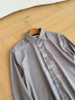 Camicia grigia elegante in tessuto leggero, appesa su stampo di legno, stile raffinato e sobrio
