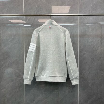 Maglietta grigia sportiva con strisce sulle maniche e colletto alto, stile casual e moderno.