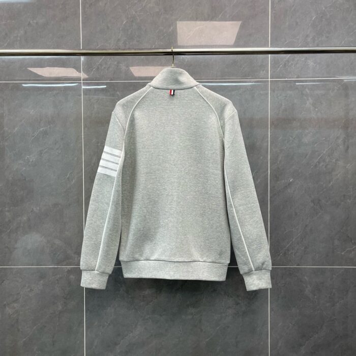Maglietta grigia sportiva con strisce sulle maniche e colletto alto, stile casual e moderno.
