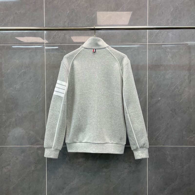 Maglietta grigia sportiva con strisce sulle maniche e colletto alto, stile casual e moderno.