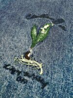 Ricamo di una foglia verde su denim, simbolo di crescita, natura e sostenibilità.