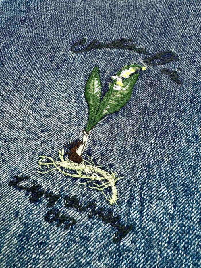Ricamo di una foglia verde su denim, simbolo di crescita, natura e sostenibilità.
