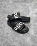 Sandali Gucci neri con logo bianco, stile casual elegante e comfort di lusso.