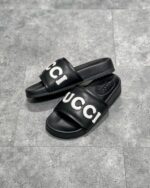 Sandali slide Gucci neri con logo bianco, stile moderno, elegante e comodo per l’estate.
