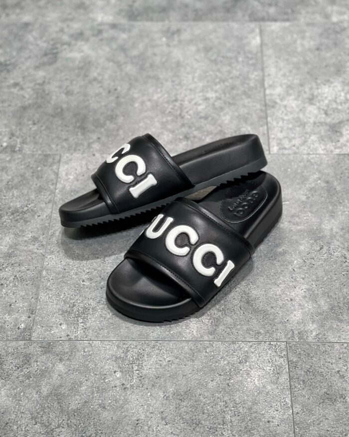 Sandali slide Gucci neri con logo bianco, stile moderno, elegante e comodo per l’estate.