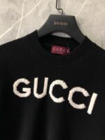 Maglione nero Gucci con logo bianco su sfondo marmo elegante e raffinato.