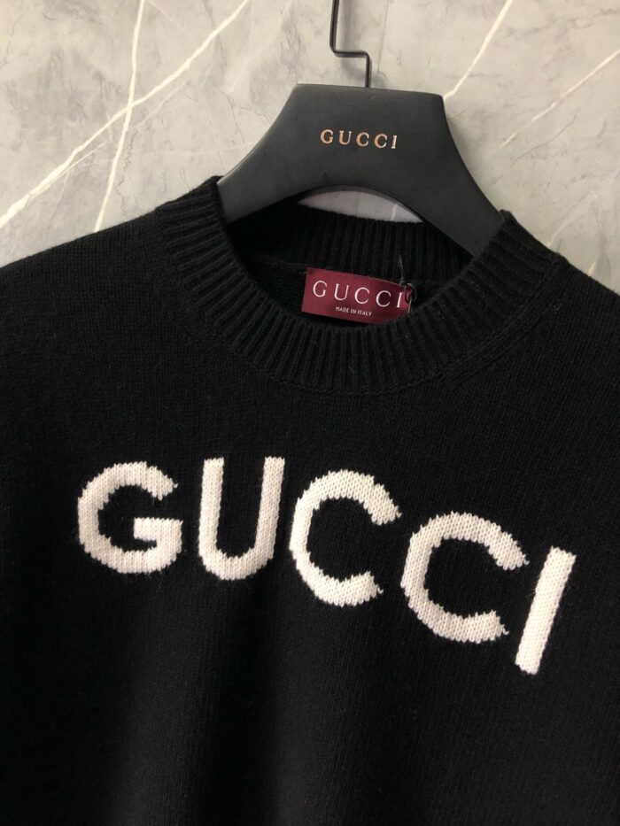 Maglione nero Gucci con logo bianco su sfondo marmo elegante e raffinato.