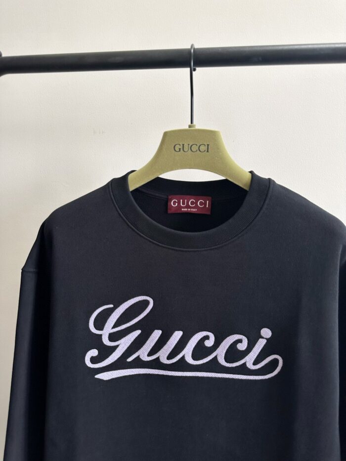 Felpa nera Gucci con logo in corsivo, esposizione minimalista su supporto sofisticato.