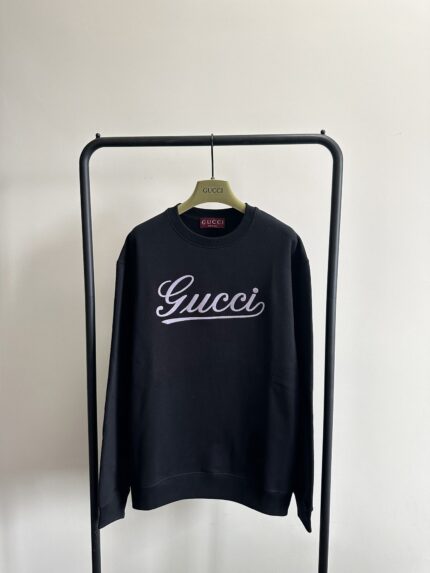 Felpa nera Gucci con logo cursivo, stile casual e raffinato su esposizione minimalista.