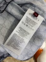 Etichetta Gucci con istruzioni di cura, logo nero e dettagli di lusso su tessuto argento.