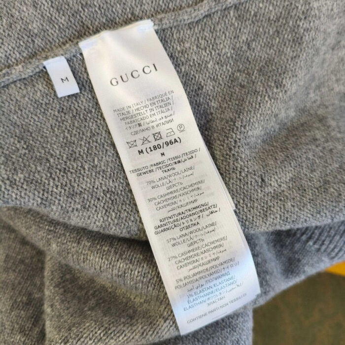 Etichetta Gucci su maglione di cachemire grigio, eleganza e qualità alta fashion.
