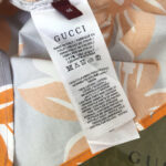Etichetta Gucci su abito estivo tropicale, dettagli di lusso e cura in italiano.