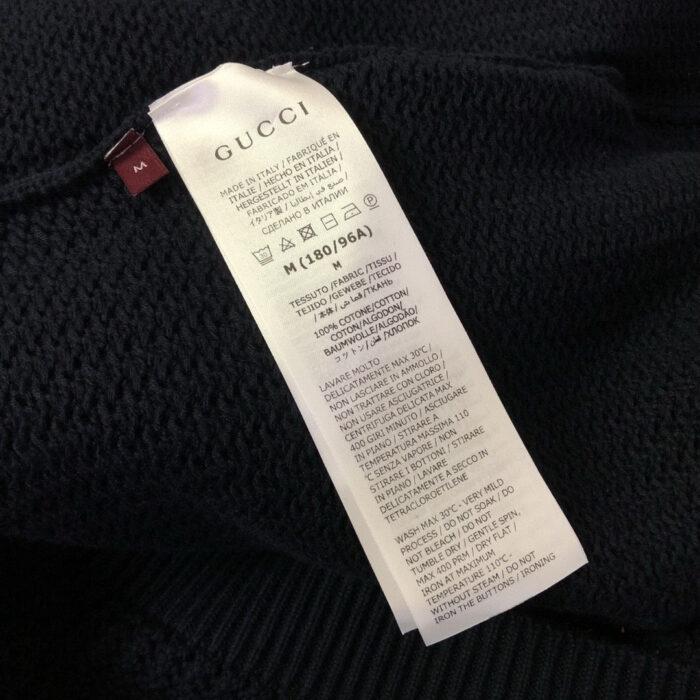 Etichetta Gucci con istruzioni di cura e taglia M su tessuto nero.
