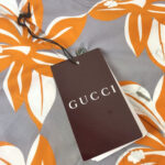 Camicia Gucci a Fiori colorati su sfondo grigio, con etichetta di lusso e bottoni eleganti.