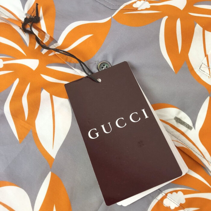 Camicia Gucci a Fiori colorati su sfondo grigio, con etichetta di lusso e bottoni eleganti.