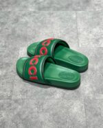 Sandali Gucci verdi con logo rosso, stile moderno, comfort e lusso su superficie grigia.