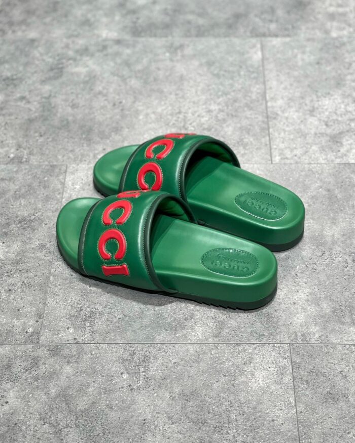 Sandali Gucci verdi con logo rosso, stile moderno, comfort e lusso su superficie grigia.