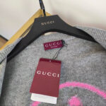 Maglione Gucci grigio con Logo rosa, etichetta marrone, su appendiabiti di legno elegante.