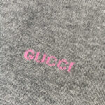 Logo Gucci rosa su tessuto grigio di alta qualità, stile elegante e moderno.