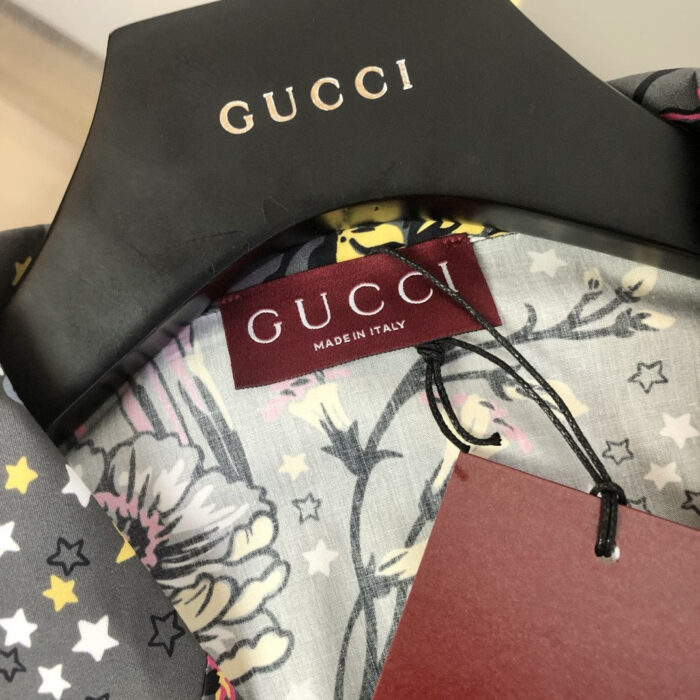 Abito Gucci con motivo floreale, logo in oro e tag di lusso italiano.