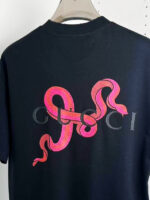 T-shirt Gucci nera con serpente rosa stilizzato e logo in grigio, stile streetwear e moda di lusso.
