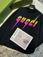 Felpa Gucci colorata con logo e brochure Jil Sander su sfondo neutro.