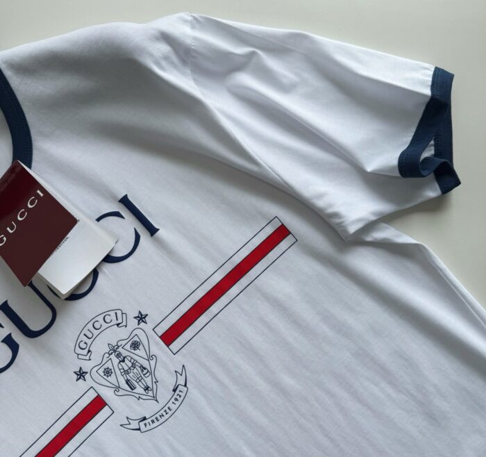 T-shirt Gucci bianco con logo, dettaglio scudo e finiture navy elegante e casual.