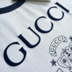 Maglietta Gucci bianca con logo e crest blu navy, stile elegante e di lusso.