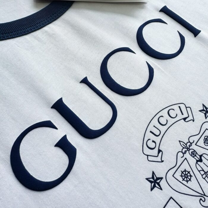 Maglietta Gucci bianca con logo e crest blu navy, stile elegante e di lusso.
