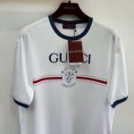 Maglietta Gucci bianca con logo Leone, strisce rosse e blu, dettagli sportivi e stile di lusso.