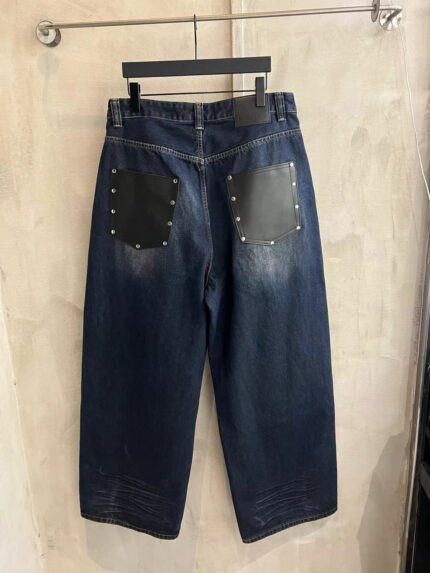 Jeans denim nero con tasche in pelle, borchie e dettagli vintage, stile streetwear moderno.