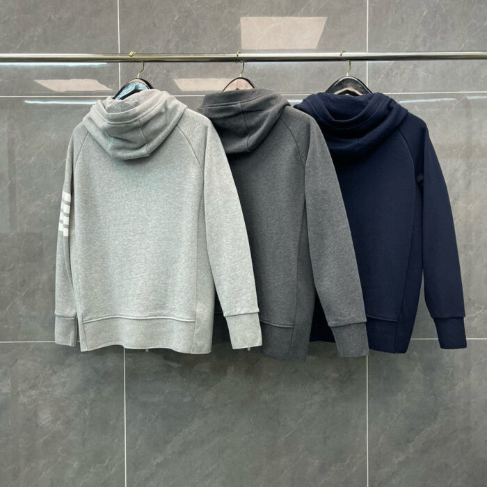Felpe con cappuccio grigie, navy e charcoal in esposizione moderna su parete di piastrelle.