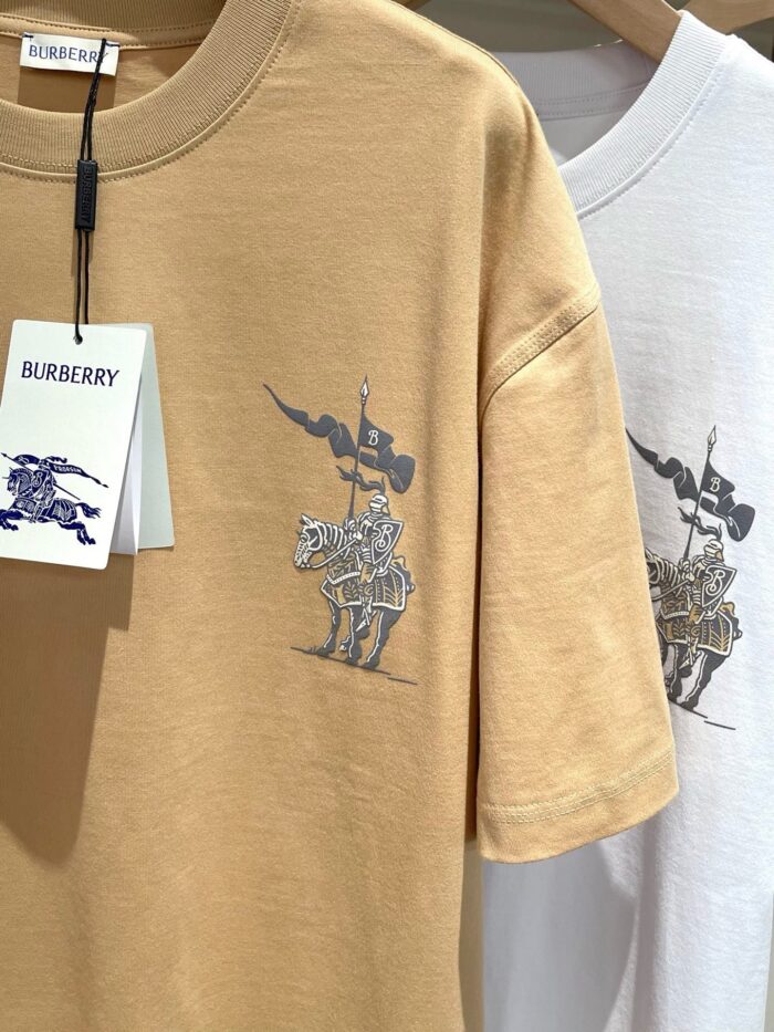 Magliette Burberry con grafica di cavaliere in beige e bianco, stile artistico e originale.