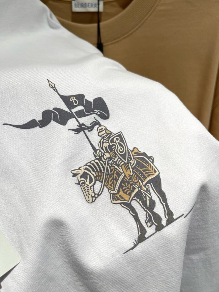 Maglietta bianca con cavaliere medievale in armatura e scudo, stile storico e valoroso.