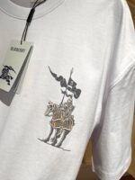 T-shirt bianca con cavaliere medievale e bandiera con lettera B, stile streetwear elegante.