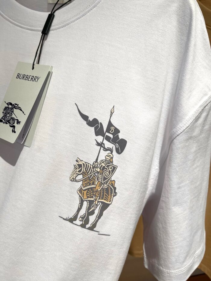 T-shirt bianca con cavaliere medievale e bandiera con lettera B, stile streetwear elegante.