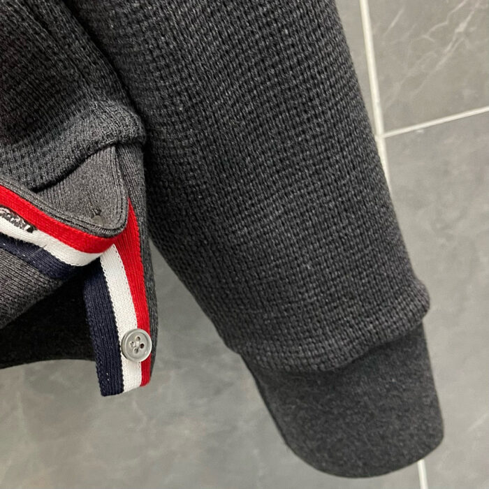 Polsino in maglia grigia con pinstripe rosse e bianche, dettagli moda casual e sportivo.