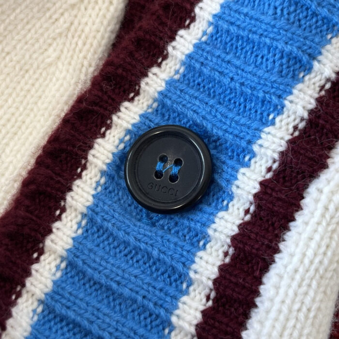 Dettaglio di maglione a strisce con bottone nero, tessuto a coste in colori rossi, blu e cream.