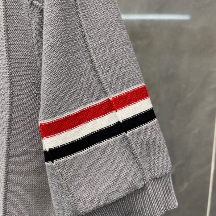 Maglione grigio con strisce sportive rosso, bianco e nero sul polsino.