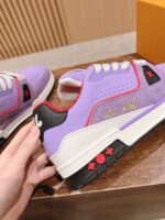 Sneakers lavanda con dettagli rossi, nero opaco e logo dorato su superficie in legno.