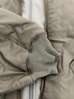 Giacca beige leggera con polsino grigio in tessuto rifinito e chiusura a zip.