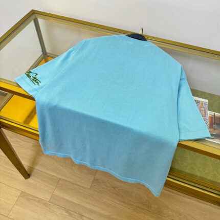 Maglietta celeste casual su tavolo in vetro, stile fresco e comfort estivo.