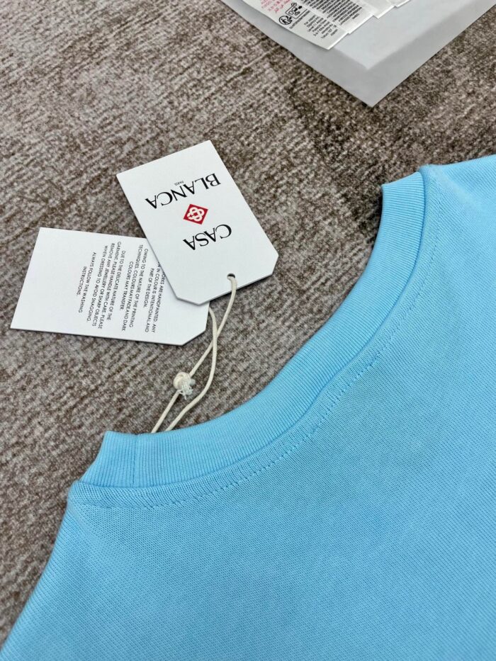 T-shirt azzurro casual con etichetta brand “CASA” e dettagli di cura.