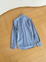 Camicia azzurra donna con colletto su pavimento in legno elegante e minimalista.