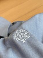 Camicia azzurra con ricamo bianco ed emblema elegante, perfetta per occasioni casual e formali.