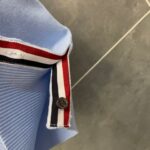 Camicia polo blu chiaro con dettagli a righe, bottoni e stile sportivo elegante.