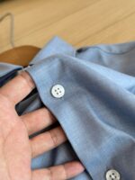 Camicia azzurra casual con bottoni e sfondo in legno, stile elegante e rilassato.