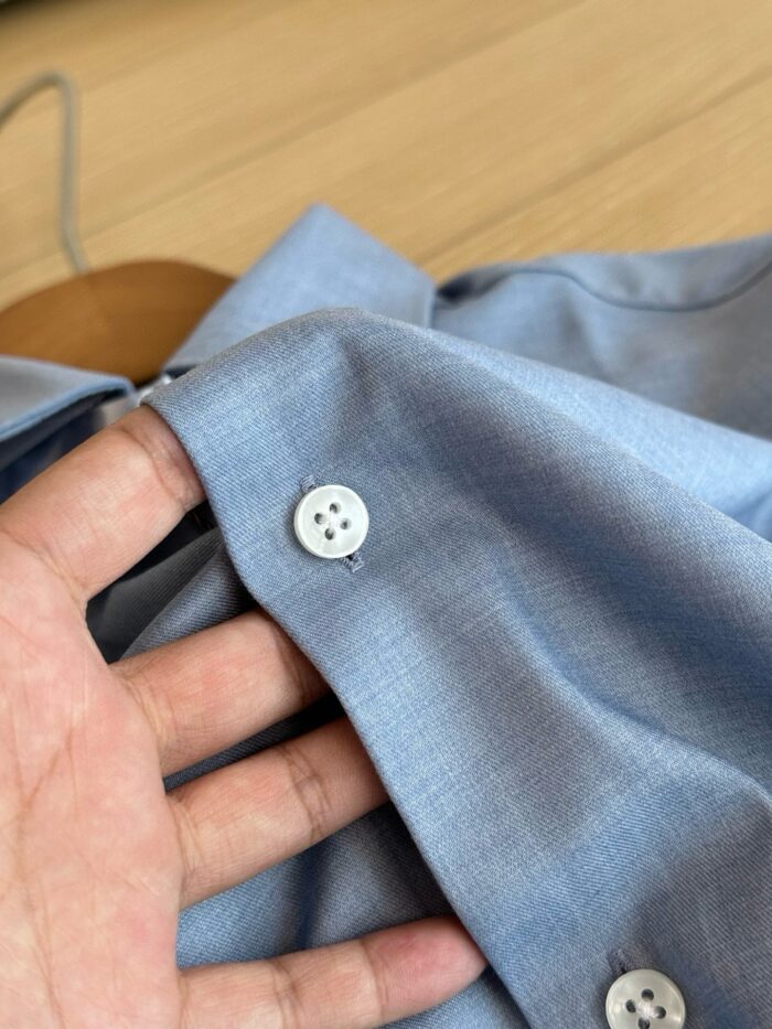 Camicia azzurra casual con bottoni e sfondo in legno, stile elegante e rilassato.