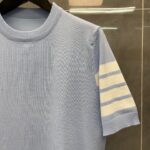 Maglietta blu chiaro con manica a righe crema, stile vintage e design elegante.